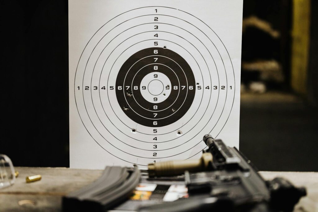 Close-up of a shooting target with bullet holes on a range table next to a rifle.